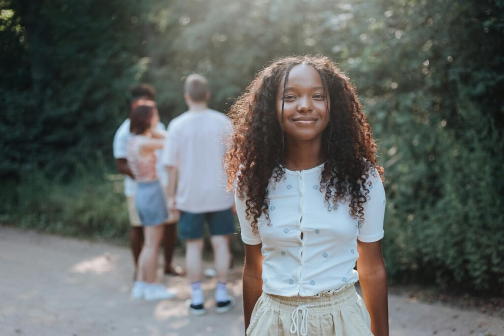 Teen girl smiling in a summer park, friends in background on a sunny day.