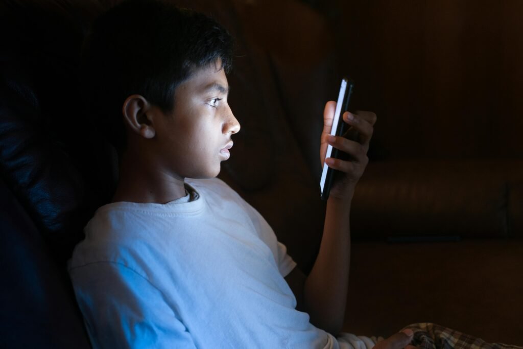 Young boy intently using a smartphone indoors at night, illuminated by screen glow.