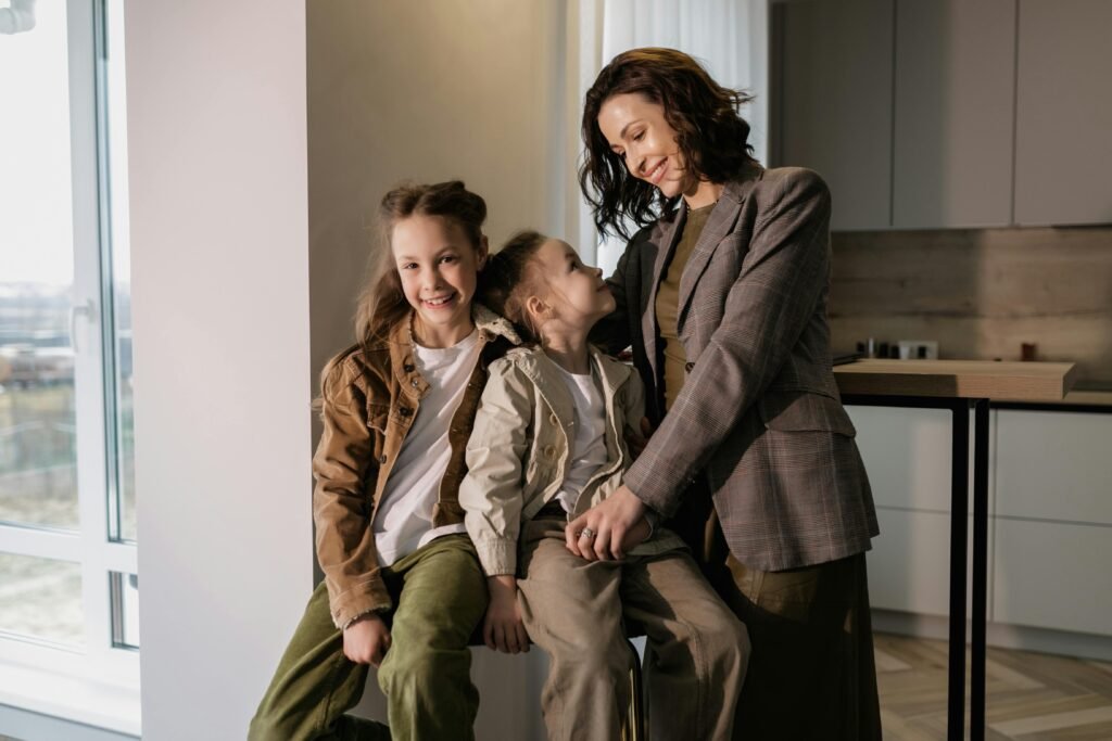A loving mother embraces her smiling daughters while sitting indoors, showcasing family warmth.